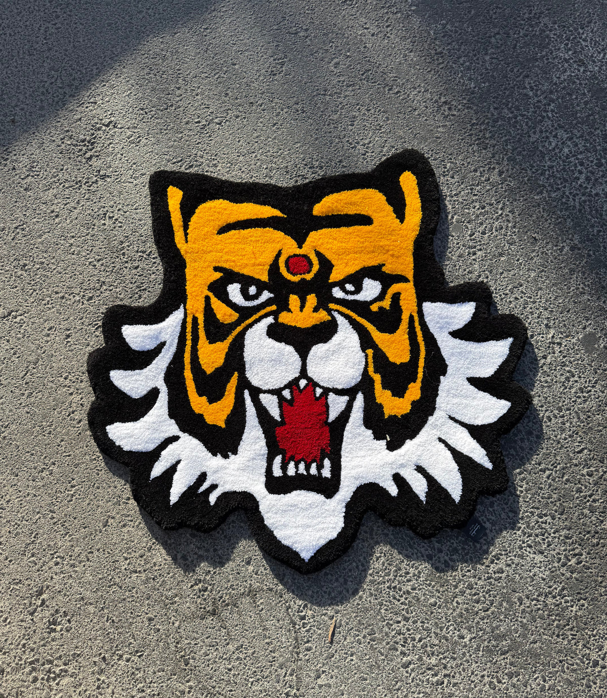 Masked Tiger tufted rug: hand-tufted tiger head rug in amber, black and white with a red gem, made in Amman, Jordan